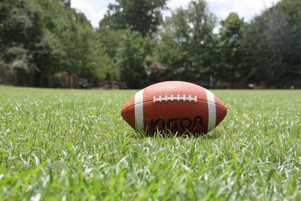 A close-up of an American football on a grassy field, highlighting outdoor sports in summer.